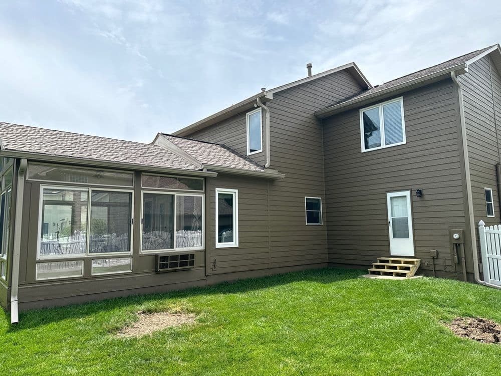 Modern brown two-story house with a screened porch and lush green lawn.